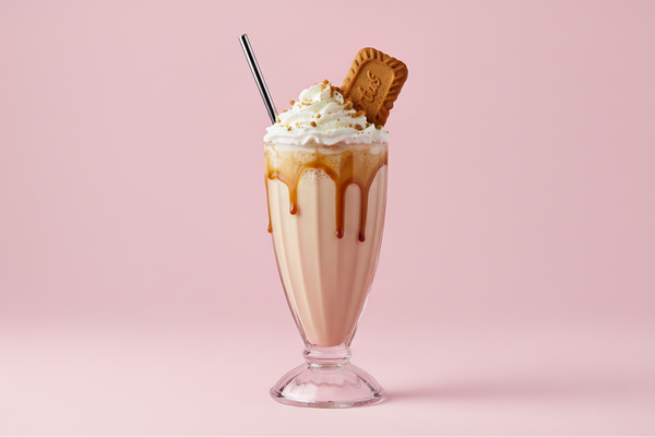 LOTUS BISCOFF SHAKE WITH 1 BISCOFF COOKIE ON THE WHIP CREAM AS GARNISH IN A MILKSHAKE GLASS WITH THE BACKGROUND BEEN #c85393